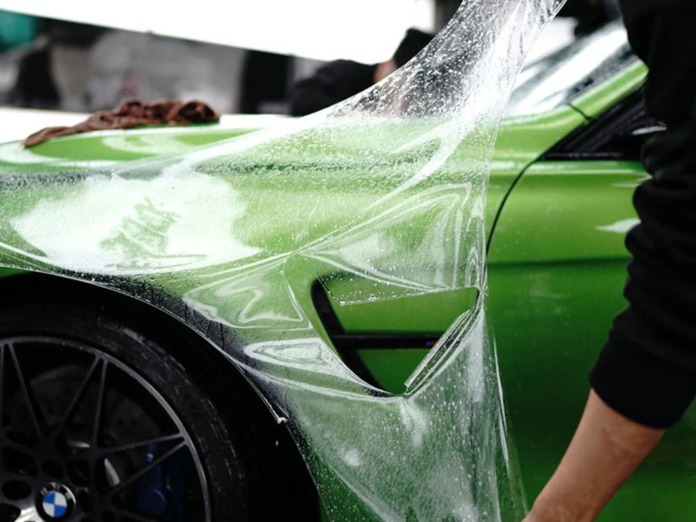 Clear paint protection film being applied to a green sports car fender