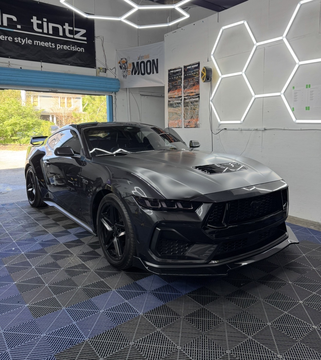 Dark grey Ford Mustang inside the Doctor Tintz bay under hexagon shop lights