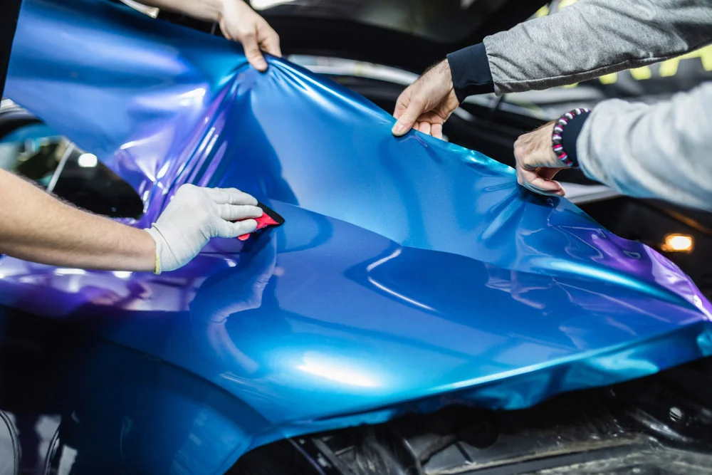 Installer applying a blue color-shift vinyl wrap to a car hood